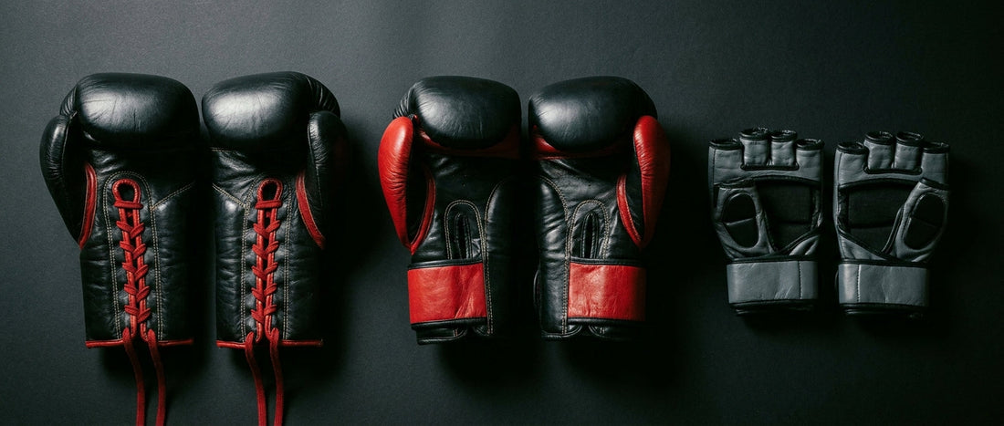 Three different types of combat sports gloves — boxing, Muay Thai, and MMA — laid out side by side on a dark surface under dramatic lighting to highlight their structural differences.