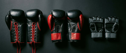 Three different types of combat sports gloves — boxing, Muay Thai, and MMA — laid out side by side on a dark surface under dramatic lighting to highlight their structural differences.
